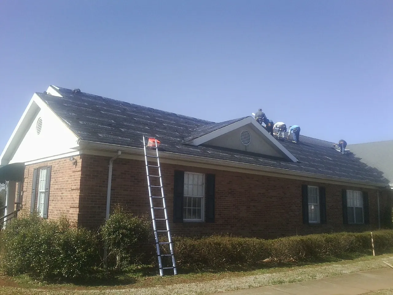 Crew tearing shingles off a brick ranch roof with a ladder set — Metal Roof Repair work by our crew in Cloverdale