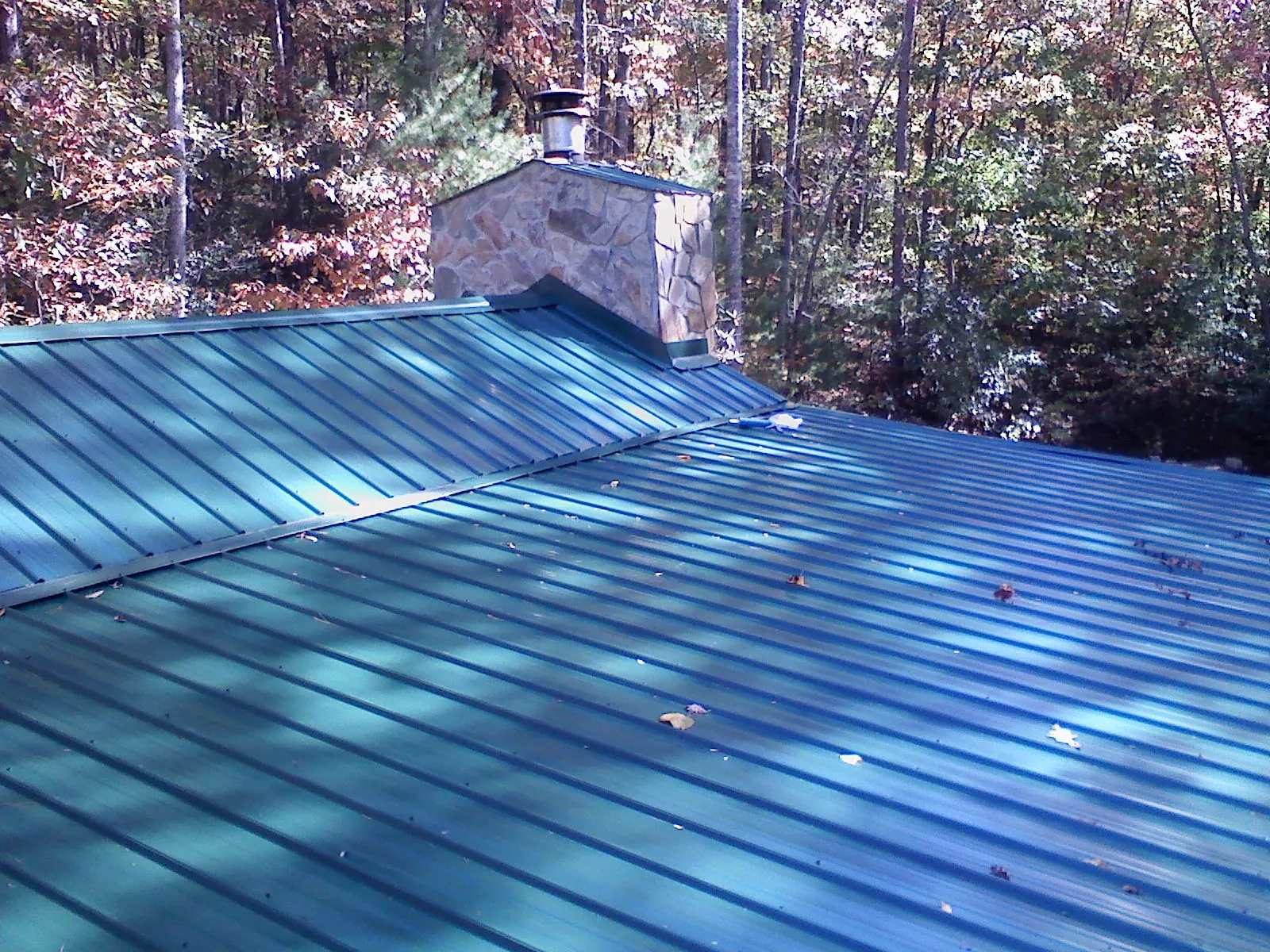 New green metal roof and stone chimney surrounded by autumn woods in Cloverdale